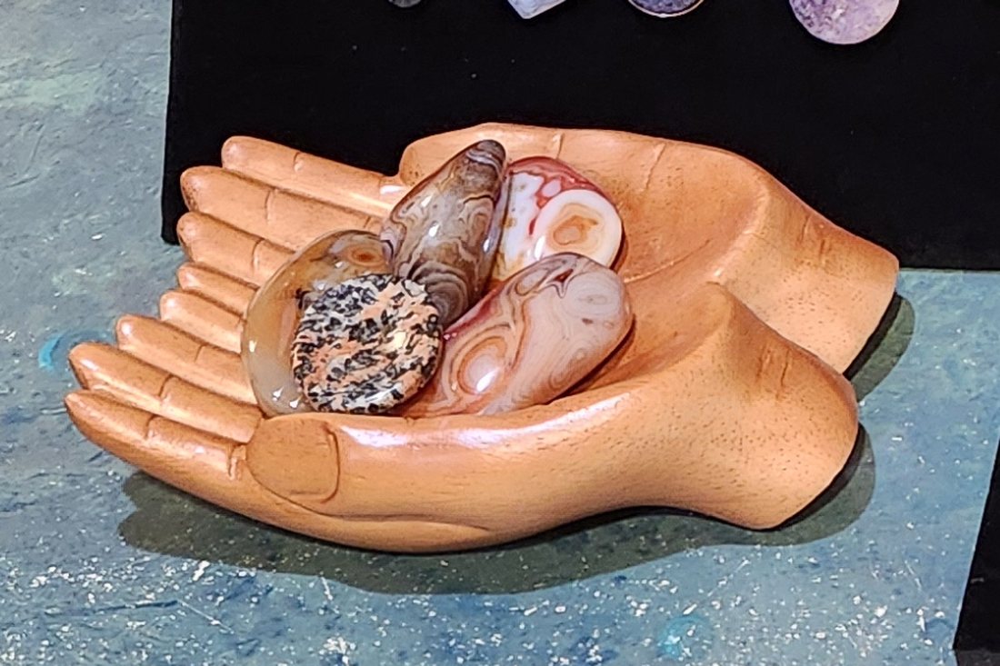 Tumbled polished stones resting in a hand-shaped wooden bowl